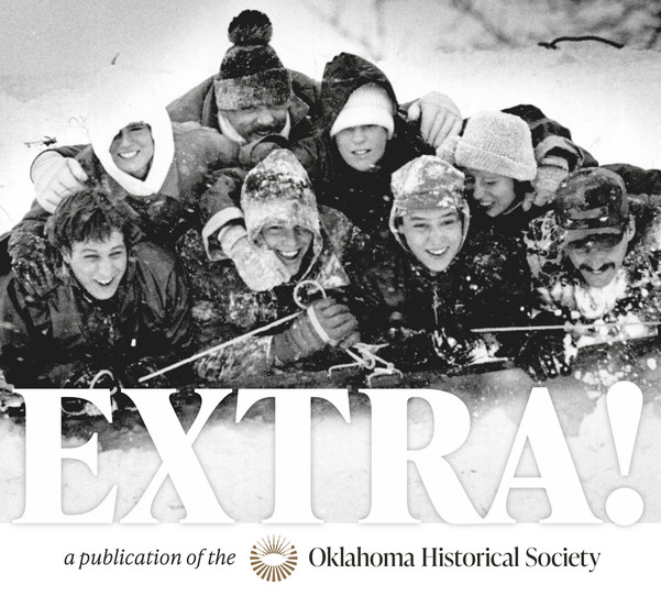 A family of eight piled in a pyramid atop a sled going downhill, snow is flying and they are all smiling