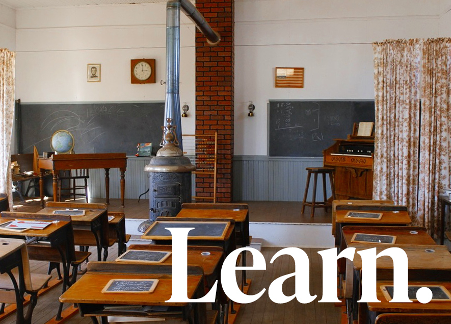 A photograph of the desks and Ben Franklin stove in the Gant one-room schoolhouse in Kingfisher. The word "Learn." appears in the right lower corner 