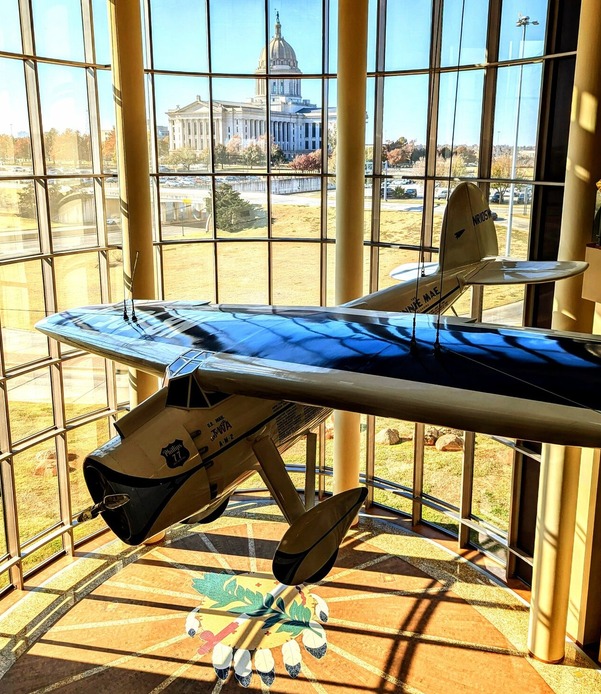 The Oklahoma History Center Devon Great Hall with a photo of the Oklahoma Capitol at a distance and the Winnie Mae airplane at center