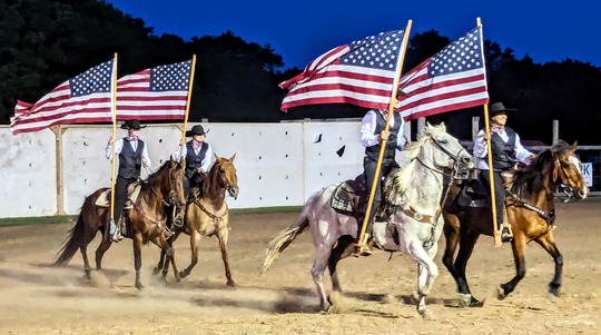 Riders in a performance at the Pawnee Bill Wild West Show, riding horseback in uniforms with American flags streaming