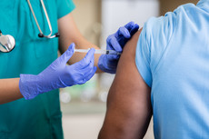 A clinician injecting the arm of a man with his sleeve rolled up