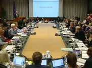 A large group of participants seated around a table watching a slide presentation.